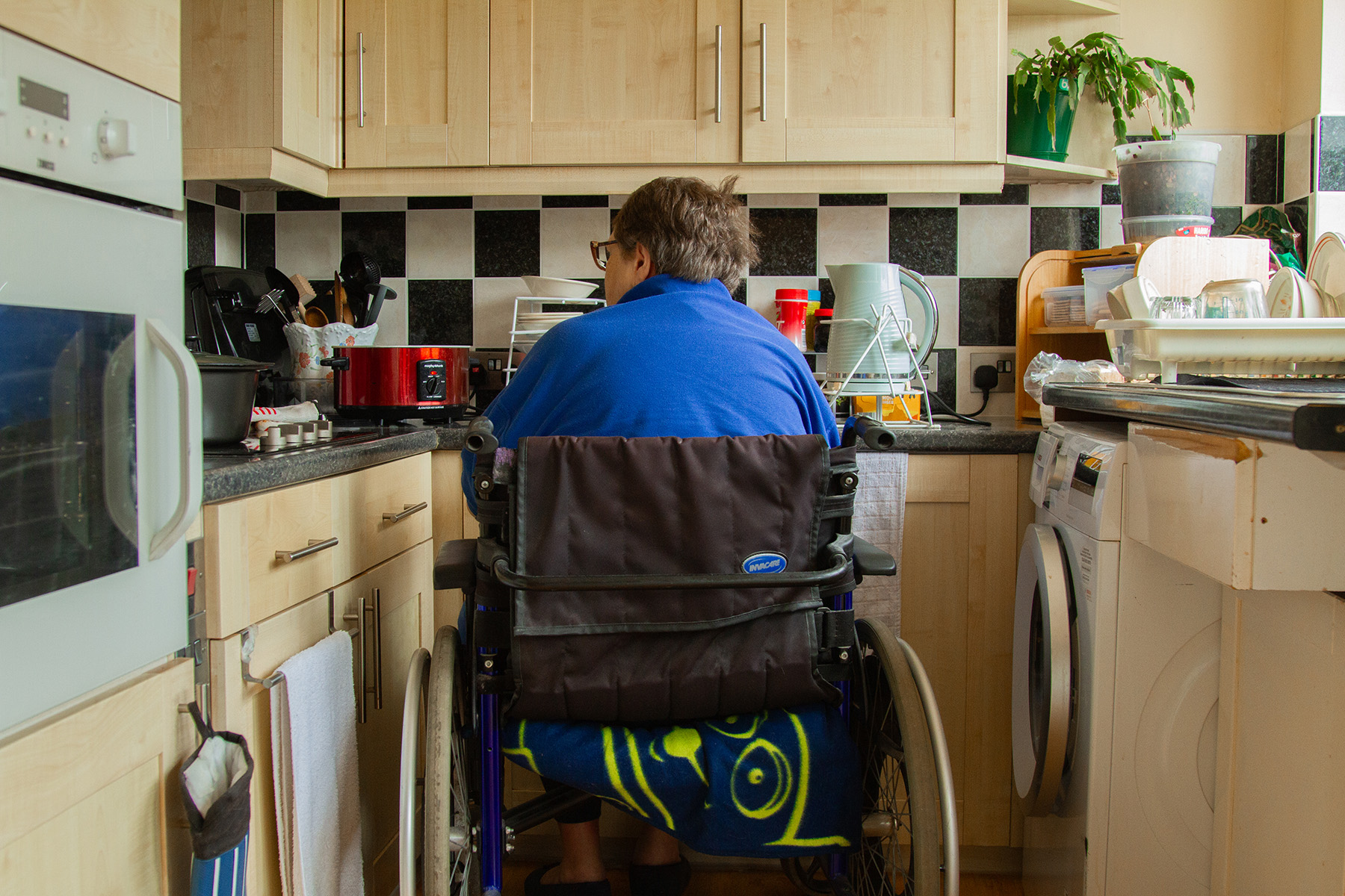 Photographie qui illustre l'analyse de l'Observatoire sur le crédit d'impôt pour maintien à domicile des aînés. On y voit une personne aînée vue de dos dans son fauteuil roulant, en train de s'affairer dans sa cuisine.