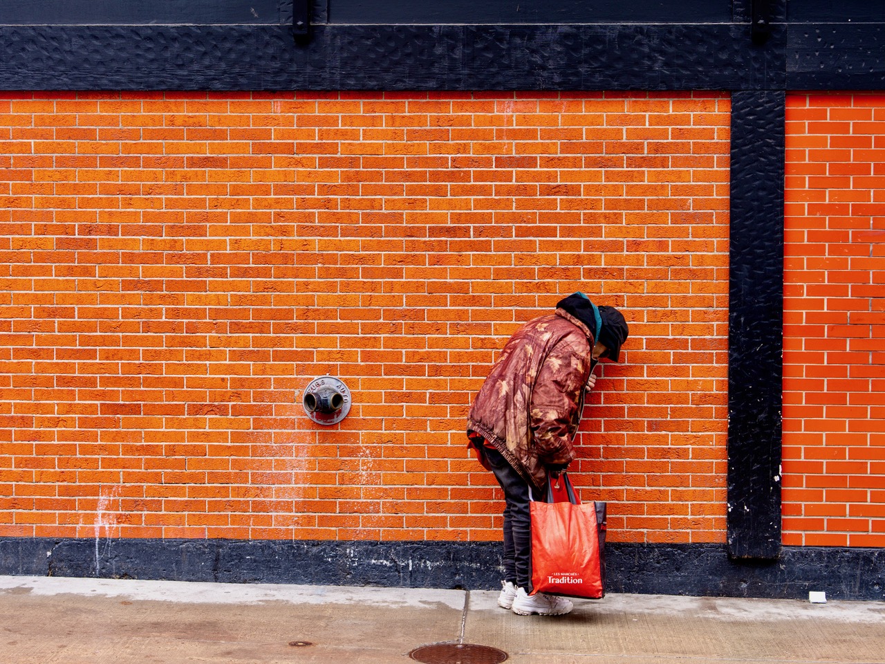 Photographie utilisée pour illustrer l'article sur la perception de la pauvreté. On y voit une personne sans domicile qui se protège du froid face à un mur de briques.